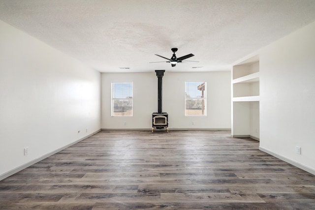 unfurnished living room featuring a wood stove, ceiling fan, dark wood finished floors, and a textured ceiling