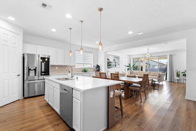 kitchen with appliances with stainless steel finishes, white cabinetry, sink, hanging light fixtures, and a center island with sink