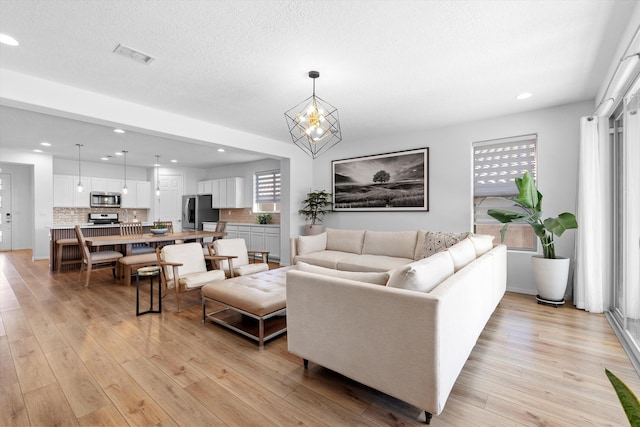 living room featuring a notable chandelier, light hardwood / wood-style floors, and a textured ceiling