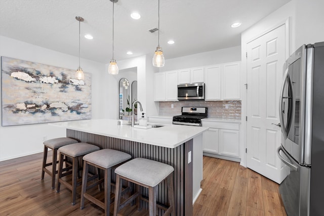 kitchen featuring appliances with stainless steel finishes, white cabinetry, sink, hanging light fixtures, and a kitchen island with sink