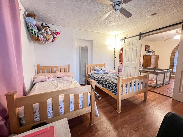 bedroom with hardwood / wood-style flooring, ceiling fan, a barn door, and a textured ceiling