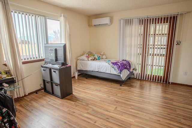 bedroom with a textured ceiling, a wall unit AC, and light wood-type flooring