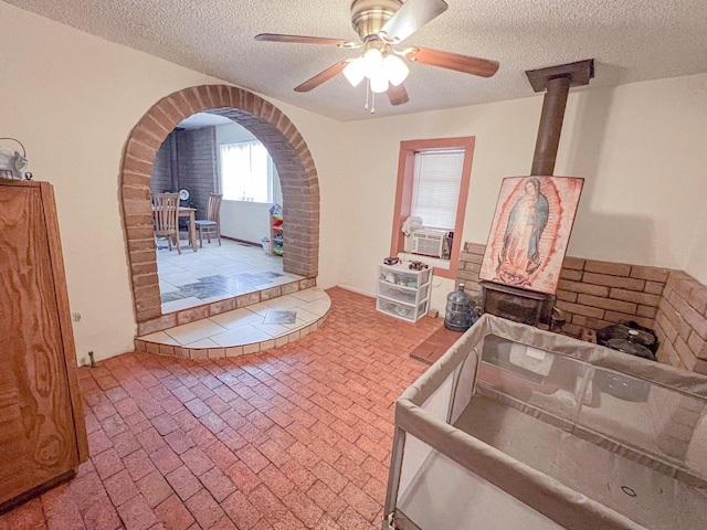 interior space with cooling unit, a textured ceiling, ceiling fan, and a wood stove