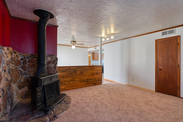 carpeted living room with crown molding, a wood stove, ceiling fan, and a textured ceiling