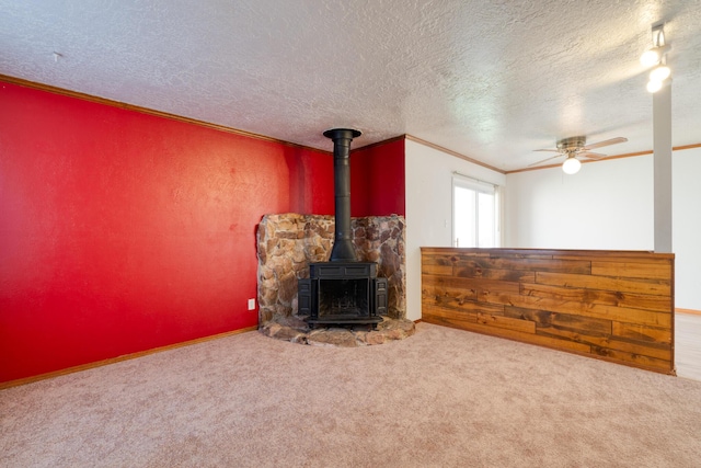 unfurnished living room featuring crown molding, a textured ceiling, a wood stove, ceiling fan, and carpet