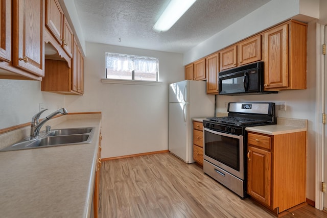 kitchen featuring sink, white refrigerator, light hardwood / wood-style floors, gas stove, and a textured ceiling