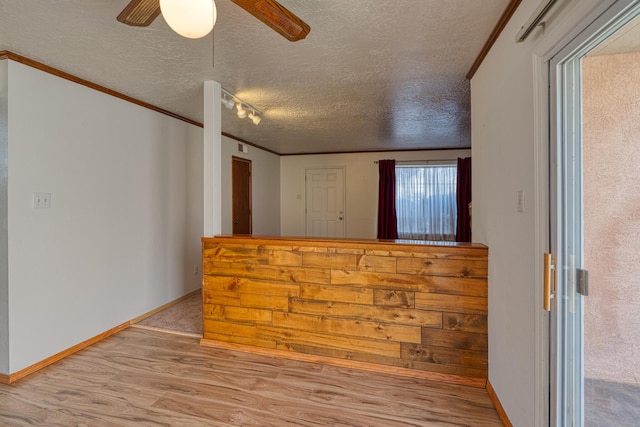 empty room featuring rail lighting, light wood-type flooring, ceiling fan, crown molding, and a textured ceiling