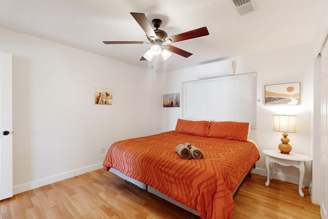 bedroom featuring ceiling fan, a wall unit AC, and light hardwood / wood-style flooring