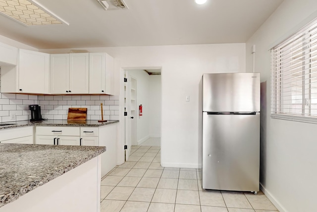 kitchen with white cabinetry, dark stone counters, stainless steel fridge, and decorative backsplash