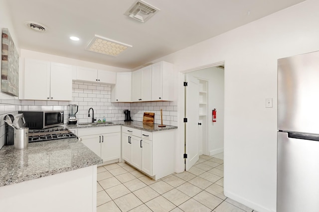 kitchen with sink, appliances with stainless steel finishes, light stone counters, white cabinets, and decorative backsplash