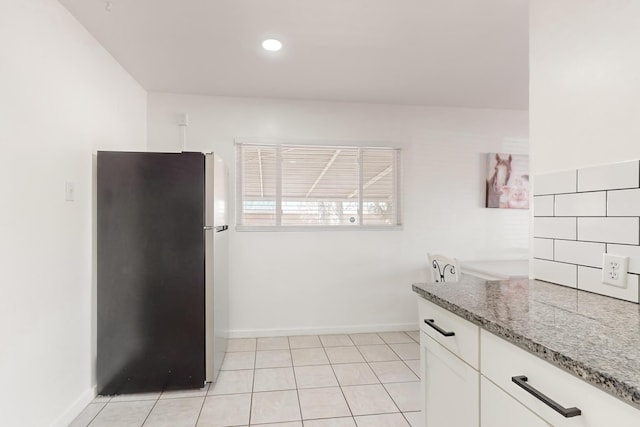 kitchen with white cabinetry, light stone countertops, light tile patterned floors, and stainless steel fridge