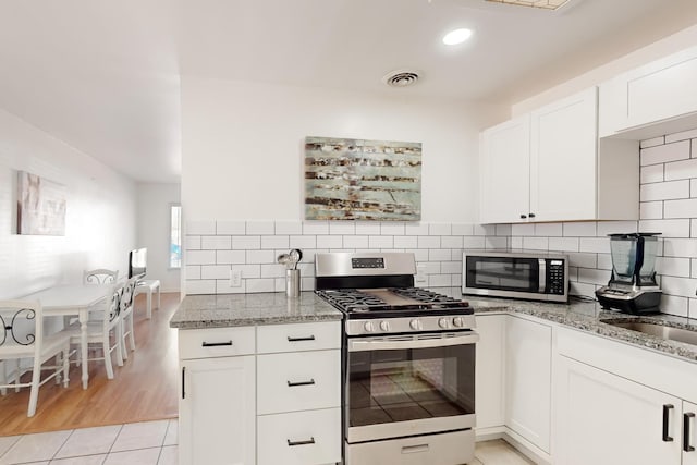 kitchen featuring appliances with stainless steel finishes, white cabinets, light stone counters, and decorative backsplash