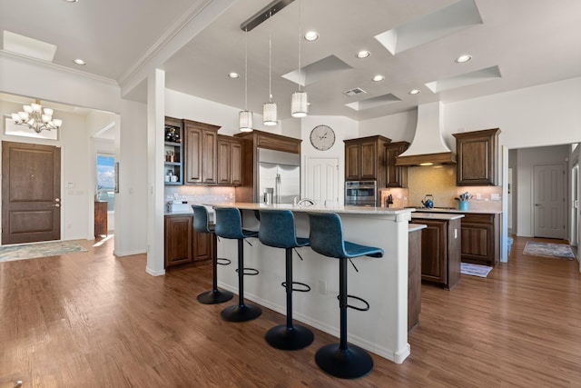 kitchen featuring pendant lighting, appliances with stainless steel finishes, a kitchen island with sink, a kitchen breakfast bar, and custom range hood