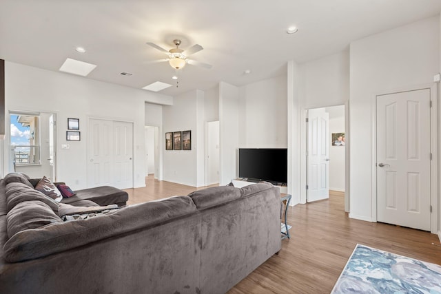 living room featuring a skylight, ceiling fan, and light wood-type flooring