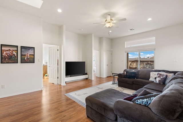 living room with ceiling fan, a skylight, and light wood-type flooring