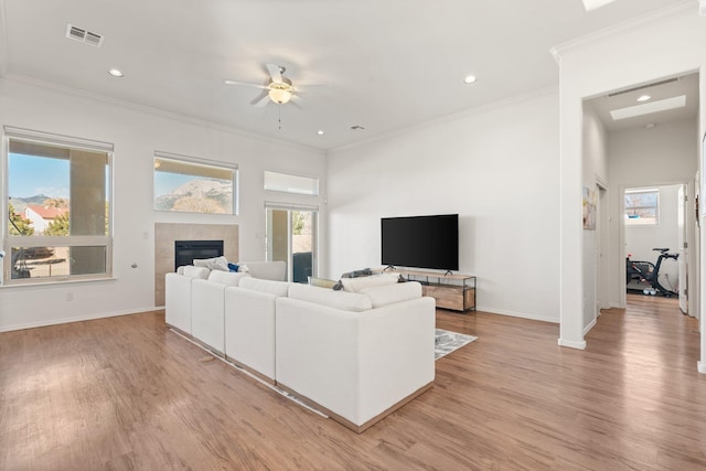 living room featuring a tiled fireplace, crown molding, a wealth of natural light, and light wood-type flooring