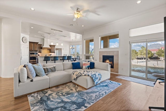 living room featuring light hardwood / wood-style flooring, ornamental molding, a tile fireplace, and a healthy amount of sunlight