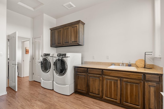 laundry room featuring cabinets, sink, washer and dryer, and light hardwood / wood-style flooring