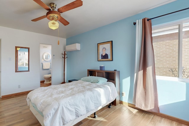 bedroom with ensuite bathroom, a wall mounted AC, ceiling fan, and light hardwood / wood-style floors