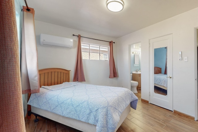 bedroom with sink, ensuite bathroom, an AC wall unit, and light wood-type flooring