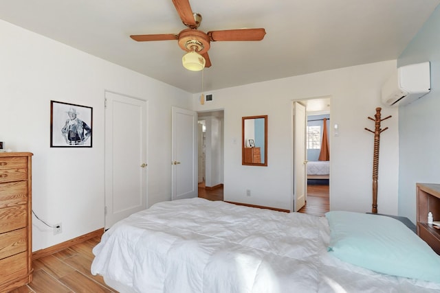 bedroom with ceiling fan, a wall mounted AC, and light wood-type flooring