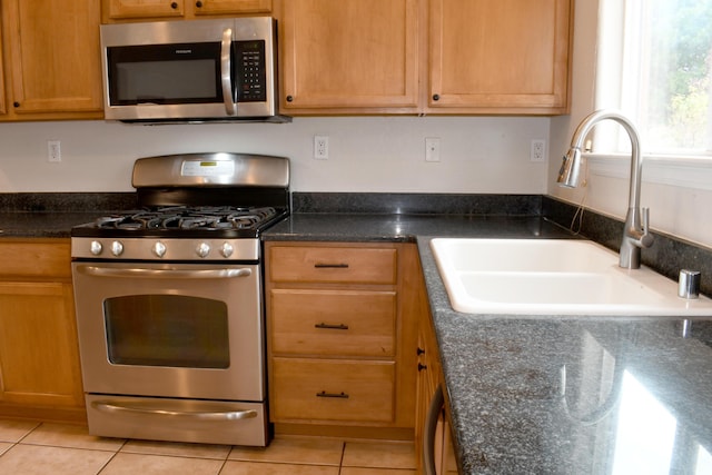 kitchen featuring sink, light tile patterned floors, dark stone counters, and appliances with stainless steel finishes