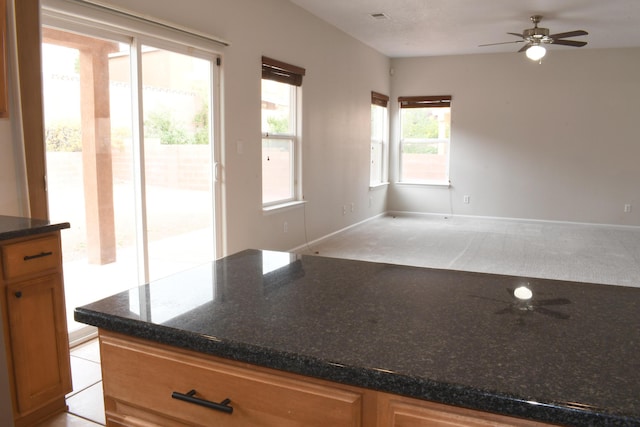 kitchen featuring ceiling fan and dark stone countertops