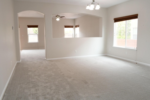 carpeted spare room featuring ceiling fan with notable chandelier