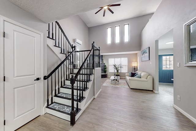 staircase with a towering ceiling, a wall mounted AC, hardwood / wood-style flooring, ceiling fan, and a textured ceiling