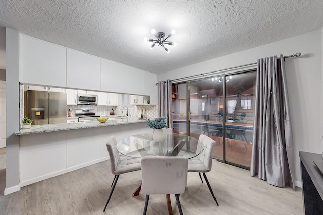 dining room with sink, a textured ceiling, a chandelier, and light hardwood / wood-style flooring