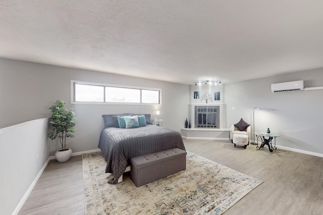 bedroom with hardwood / wood-style flooring, a textured ceiling, and a wall unit AC