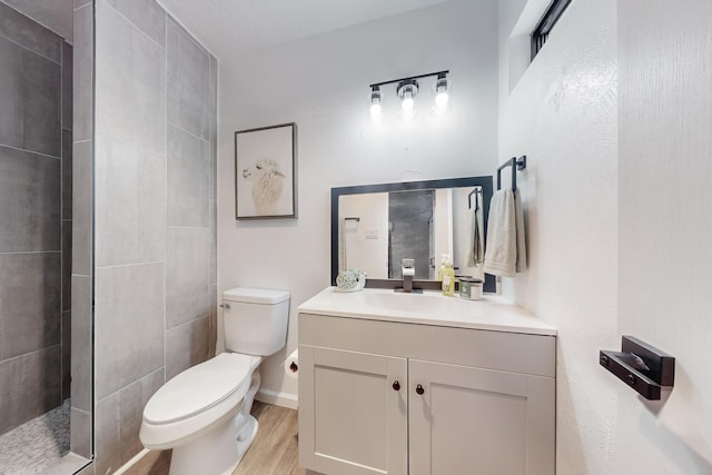 bathroom featuring hardwood / wood-style flooring, vanity, a tile shower, and toilet