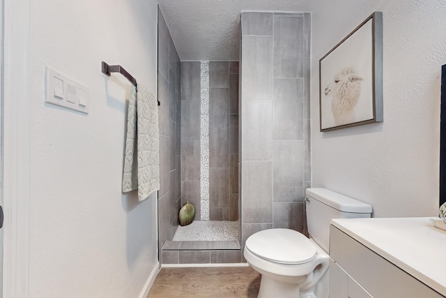 bathroom featuring vanity, hardwood / wood-style flooring, toilet, and tiled shower