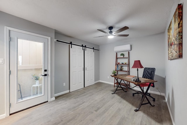 office space with a wall mounted air conditioner, light hardwood / wood-style flooring, a barn door, and ceiling fan