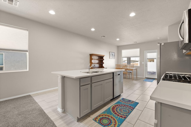 kitchen with gray cabinets, an island with sink, sink, stainless steel appliances, and a textured ceiling