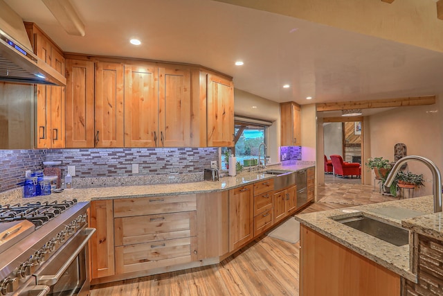 kitchen with tasteful backsplash, sink, wall chimney range hood, and light stone counters