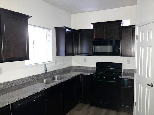 kitchen featuring sink, dark wood-type flooring, light stone counters, and black appliances