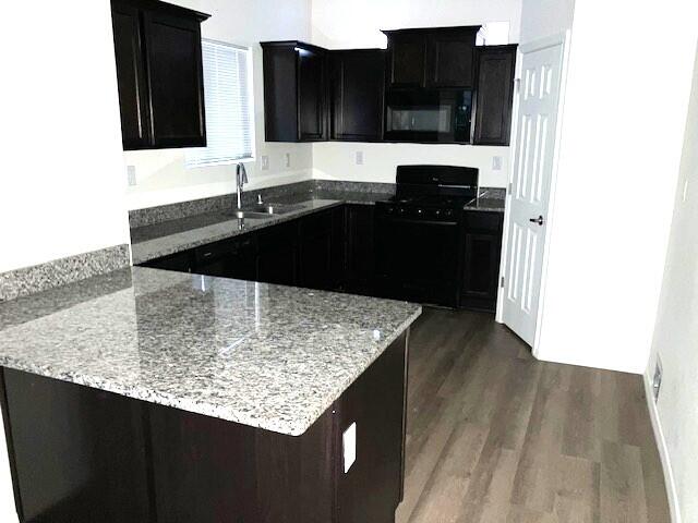 kitchen with light stone countertops, sink, black appliances, and dark hardwood / wood-style floors