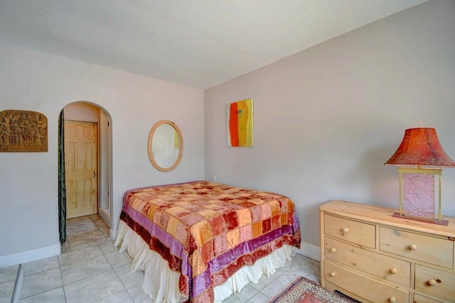 bedroom featuring arched walkways, baseboards, and light tile patterned flooring