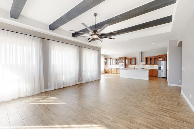 unfurnished living room with beamed ceiling, ceiling fan, sink, and light hardwood / wood-style flooring