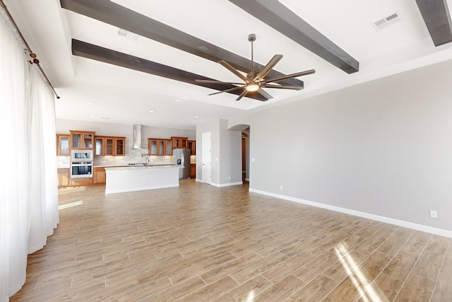 unfurnished living room featuring beam ceiling, ceiling fan, and light hardwood / wood-style floors