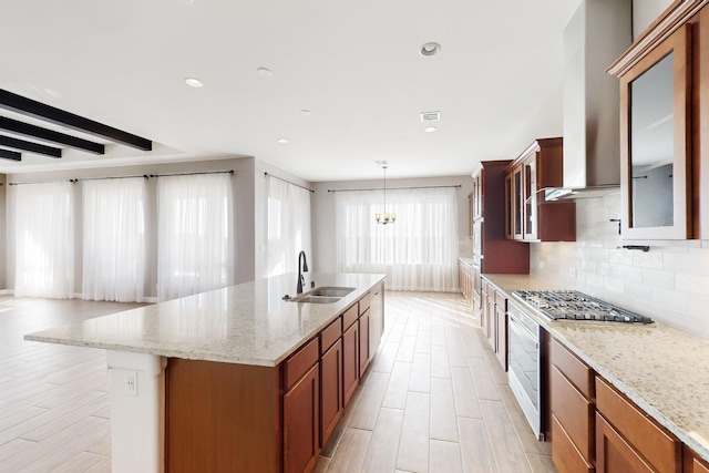 kitchen with stainless steel gas stovetop, tasteful backsplash, sink, a kitchen island with sink, and light stone counters