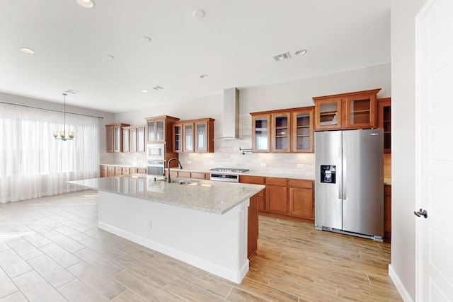 kitchen with tasteful backsplash, a center island with sink, appliances with stainless steel finishes, light stone countertops, and wall chimney range hood