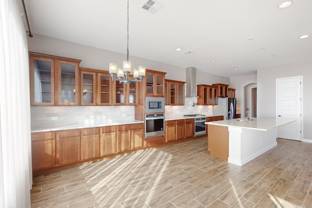 kitchen with wall chimney exhaust hood, tasteful backsplash, hanging light fixtures, an island with sink, and stainless steel appliances