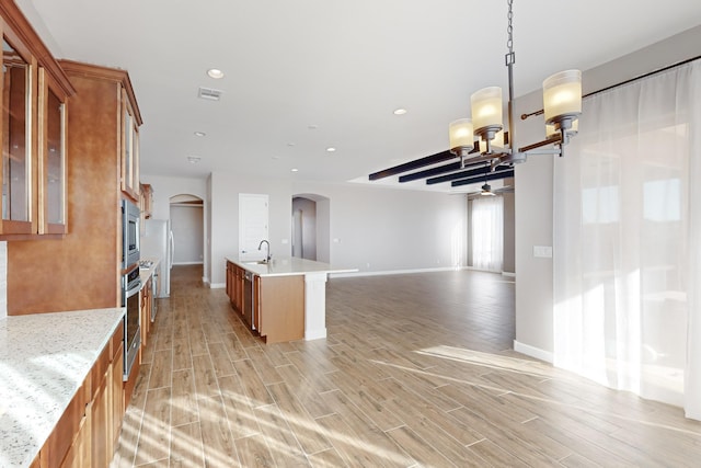 kitchen with sink, hanging light fixtures, appliances with stainless steel finishes, an island with sink, and ceiling fan with notable chandelier