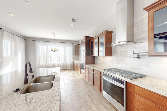 kitchen with sink, stainless steel appliances, light stone counters, decorative light fixtures, and wall chimney exhaust hood