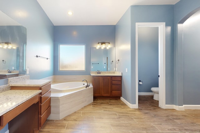 bathroom featuring vanity, a relaxing tiled tub, and toilet