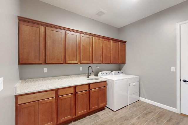 laundry area featuring cabinets, sink, washing machine and clothes dryer, and light hardwood / wood-style flooring