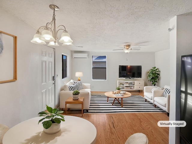 living room featuring wood-type flooring, ceiling fan with notable chandelier, a wall unit AC, and a textured ceiling