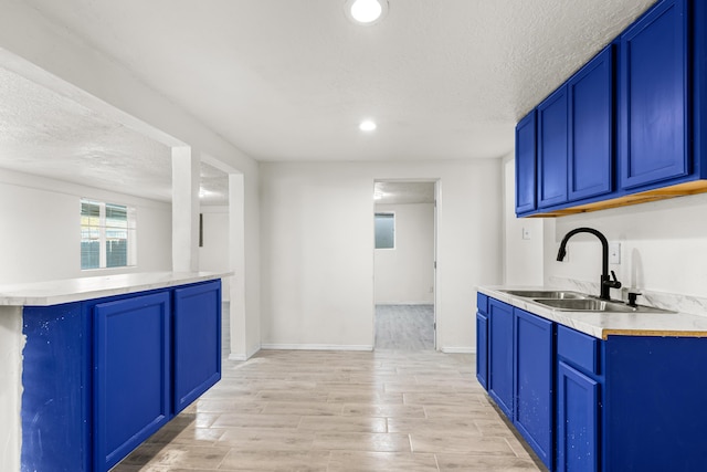 kitchen featuring blue cabinets, sink, a textured ceiling, and light hardwood / wood-style flooring